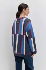 Cardigan de punto con diseño de bloques de color en azul, rojo y crema. Presenta cuello en V, cierre frontal con botones, mangas largas y dos bolsillos delanteros con bordado de cerezas.