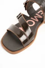 Sandalias de cuero charolado negro con dos tiras con hebillas metálicas plateadas y tira en el talón. Suela plana color marrón.