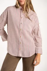 Camisa de corte oversize con estampado de rayas verticales, cuello clásico, cierre frontal con botones y bolsillo en el pecho. Presenta mangas largas con puños abotonados y un diseño fluido.