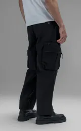 Pantalón cargo oversize de corte relajado, confeccionado en textil técnico resistente de color negro. Presenta bolsillos laterales cargo de gran tamaño con cierres metálicos, bolsillos laterales superiores y bolsillos traseros con broches a presión. Incluye cinturón integrado de cinta de seguridad con hebilla de encastre técnica.