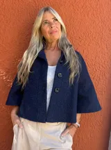 Capa corta de tejido de bucle en color azul, con corte en A, mangas raglán y cierre frontal con tres botones grandes.