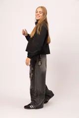 Campera negra de cuello alto con cierre frontal de cremallera y solapa con botones metálicos. Presenta mangas largas con puños elásticos y diseño vanguardista.