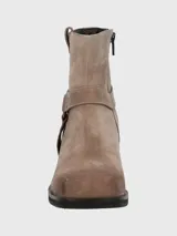 Bota corta de descarne color beige, con taco cuadrado y punta cuadrada. Presenta una correa con argolla metálica decorativa alrededor del tobillo y cierre lateral.