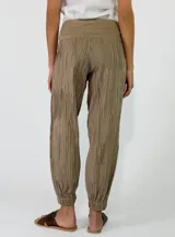 Pantalón beige con textura arrugada, de corte holgado estilo balloon con puños elásticos en los tobillos y cintura alta con faja y lazo ajustable.
