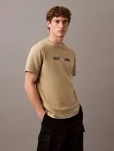 Remera de algodón con cuello redondo y manga corta, color beige. Presenta un estampado frontal con el logo de Calvin Klein y la inscripción New York en estilo cursivo.