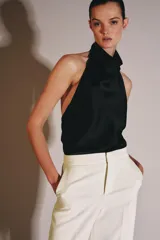 Top de cuello halter con escote fluido y caída suave. Presenta cierre con botones en la parte posterior y diseño sin mangas.