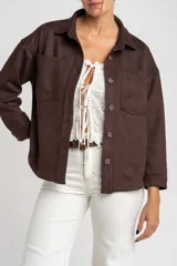 Sobrecamisa marrón de gamuza sintética con calce oversize, cuello camisero, cierre con botones a presión, mangas largas con puños abotonados y bolsillos de parche en el pecho.