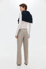 Pantalón sastrero de sarga color beige, con cintura clásica, trabillas para cinto y cierre frontal oculto. Presenta bolsillos laterales al bies, pliegues frontales y piernas rectas con raya marcada.