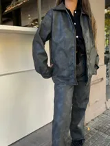 Campera de cuero sintético color gris oscuro, con cuello camisero, cierre frontal con cremallera dorada y bolsillos laterales.