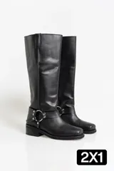 Botas de caña alta confeccionadas en cuero negro, con diseño de estilo western que incluye una correa decorativa con argollas metálicas y remaches en el tobillo. Presentan una puntera cuadrada y un taco bajo cuadrado.