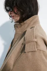 Cazadora de corte bomber en color marrón claro, con cuello subido, mangas largas con trabillas en los hombros, y cierre frontal oculto con cremallera y botones a presión.