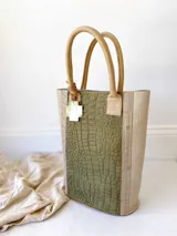 Bolso matero verde con textura croco y detalles en beige. Tiene doble asa corta y accesorio metálico en forma de cruz.