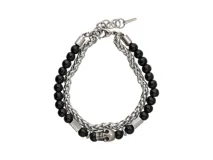 Pulsera doble de acero plateado, con una hilera de cuentas de ónix negro y otra de cadena. Incluye un dije de calavera plateada y cierre de gancho.