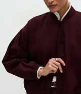 Campera estilo bomber de sarga color bordó, con cuello alto, cierre frontal con botones forrados, mangas largas con puños elásticos y bajo ajustado.