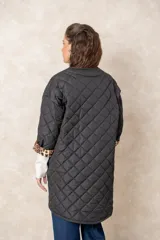 Campera acolchada de corte amplio y largo midi, color beige con diseño capitoneado. Presenta mangas tres cuartos con puños vueltos que revelan un interior estampado con motivo animal print. Diseño sin cuello y cierre frontal oculto.