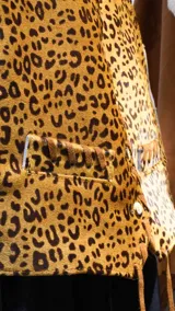 Chaleco sastrero de cuero con estampado animal print, escote en V y bolsillos frontales ribeteados. Presenta detalles de pasamanería en cuero en los bordes y cordones colgantes en el ruedo.