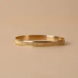Esclava rígida de oro 18k con acabado satinado y diseño de cinta plana. Presenta una textura fina en su superficie y un diseño minimalista.