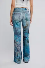 Jean de tiro medio y pierna flare de denim azul con estampa en toda la prenda y detalles de calados bordados florales en la parte inferior. Cuenta con cinco bolsillos y cierre frontal con cremallera.