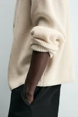 Cárdigan de punto color crema, con cuello pico, manga larga y cierre frontal de botones marrones. Presenta un calce relajado y acabados en rib.