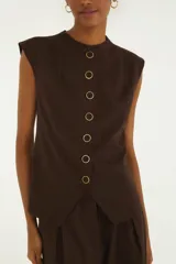 Chaleco de sastrería color marrón con finas rayas, cuello redondo, hombros estructurados y cierre frontal de botones metálicos.
