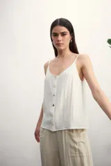 Musculosa color blanco roto con escote en V y botones frontales. La tela presenta una textura arrugada o plisada.
