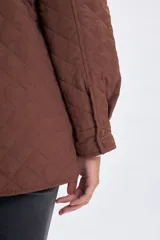 Sobrecamisa de diseño capitoneado en color marrón, con cuello clásico, cierre frontal mediante botones a presión y bolsillos frontales con solapa.