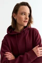 Canguro liso de color bordó, con capucha ajustable mediante cordones y bolsillo frontal tipo canguro.