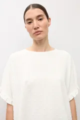Blusa crudo con textura plumetti, escote redondo y mangas cortas terminadas en delicados volados.