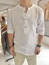 Camisa de muselina blanca de manga larga, con cuello mao y cierre frontal de botones.