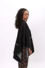 Ruana negra de corte asimétrico con detalles de costura a contraste en color blanco en los bordes. Confeccionada en tejido de algodón, presenta una caída fluida y diseño abierto.