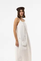 Vestido midi blanco de calce amplio y liviano, con escote regulable, breteles finos con detalles de cuentas y silueta suelta. Incluye una mini cartera al tono desmontable.