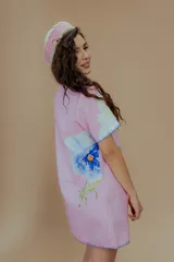 Vestido corto de lino y algodón color rosado, con cuello de solapa y manga corta. Presenta un diseño abotonado al frente con estampados de flores azules y saltamontes verdes, además de detalles de bordado a mano en contraste azul en los bordes.