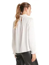 Blusa de gasa labrada color blanco, con cuello alto en punto smock, mangas largas con terminación fruncida y diseño elegante.