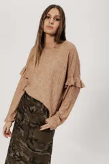 Buzo color beige de punto con lanilla tipo canelón, corte holgado y mangas largas con volados en los hombros.