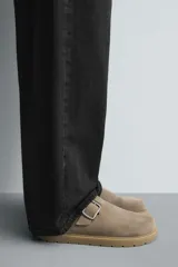 Zueco tipo mule de hombre, color beige topo, fabricado en piel con acabado serraje. Presenta una tira con hebilla metálica cuadrada en el empeine y suela gruesa de goma en color natural contrastante.