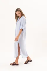 Vestido camisero largo color celeste, de silueta relajada con abotonadura frontal completa, cuello camisero y mangas regulables. Presenta tajos laterales y detalle de bordado sutil en la manga.