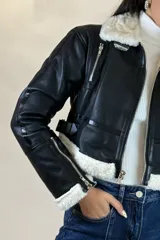 Campera tipo gamulán de cuero sintético negro, con interior y detalles de cuello y puños en corderito blanco. Presenta cierre frontal, cierres en los puños y correas ajustables en la cintura.