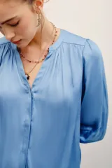 Camisa de poliéster color beige, con escote en V profundo, mangas 3/4 abullonadas y diseño fluido.