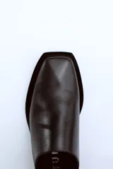 Mocasín negro de cuero con punta cuadrada y talón descubierto.