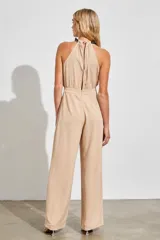 Mono largo color nude de silueta relajada, con escote halter y detalle de cadena negra en el cuello que aporta un toque sofisticado y moderno.