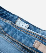 Pantalón de jean femenino azul claro, modelo flare, con silueta ajustada en caderas y muslos, y acampanado desde la rodilla. Cuenta con cintura media, cierre de botón y cremallera, bolsillos delanteros curvos y bolsillos traseros tradicionales. Confeccionado en algodón más sostenible con elastano.