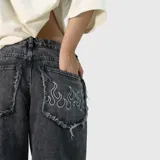 Pantalón de jean estilo baggy, color negro con efecto lavado. Presenta un corte extremadamente holgado, bolsillos traseros con bordes deshilachados y un diseño de llamas bordado en uno de los bolsillos traseros.