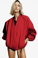 Chaqueta tipo bomber de Zara, color rojo, con escote en pico, cierre frontal cruzado con botones a presión y mangas largas abullonadas con puños elásticos. Cuenta con bolsillos delanteros y forro interior a tono.