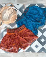 Short de seda con elástico fruncido en la cintura y volado en el ruedo. Presenta un estampado vibrante en tonos rojo/bordó y turquesa con motivos florales o arabescos.