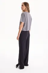 Pantalón deportivo negro de corte wide leg, sin frisa, con ribete blanco en los laterales y aberturas con botones en los tobillos.