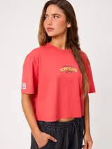 Remera coral cropped, de manga corta, con estampa trasera colorida de un perro surfeando y el texto "Rusty County Surf Club".