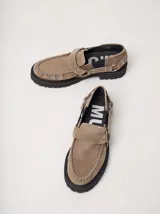 Mocasines Mutma Gales de cuero color tostado, con plataforma gruesa dentada, detalles de tachas metálicas, argollas y tira lateral con hebilla.