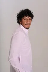 Camisa de manga larga confeccionada en tejido poplin con diseño de rayas verticales finas en color rosado y blanco. Presenta cuello abotonado (button-down), cierre frontal con botones y un bolsillo en el pecho.