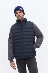 Chaleco puffer negro con diseño acolchado horizontal, cuello alto y cierre frontal. Presenta un bolsillo lateral con detalle de marca grabado.