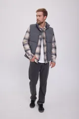 Chaleco puffer gris sin mangas con cuello alto y cierre de cremallera. Tiene bolsillos frontales y relleno de fibra sintética.